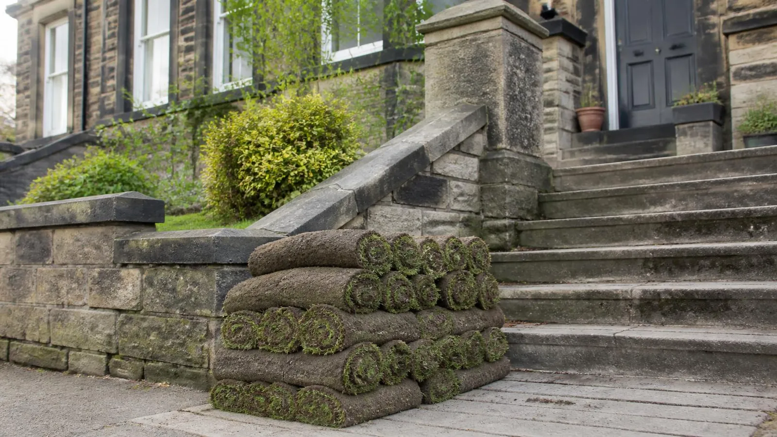 Rolls of fresh turf stacked at the foot of stone garden steps, ready to carry up